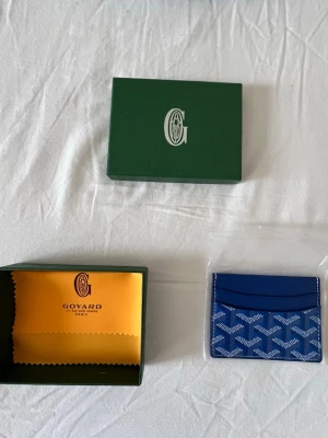 G-plånbok  - Snygg och stilren i färgen blå med deras ikoniska mönster. Plånboken har flera kortfack och är tillverkad i skinn med tryckt logga framtill. Perfekt för dig som vill ha något exklusivt och smidigt i fickan.  