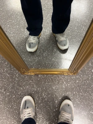 Grå vita rockrunners - Snygga sneakers i grått och vitt med meshpaneler och mockadetaljer. Skorna har vita snören, gummisula i beige och en klassisk låg siluett. Perfekta för dig som gillar stilrena och sportiga skor med modern känsla.