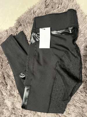 Svarta Cindy ridtights från Ps of Sweden - Snygga svarta Cindy ridtights från Ps of Sweden med mod waist och detaljer i läder. Tightsen har silikonmönster på sätet för extra grepp och är tillverkade i stretchigt funktionsmaterial som passar perfekt till ridning. Byxorna är helt oanvända och storlek 40 men passar även 38.
