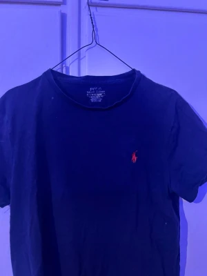 Svart t-shirt från Polo Ralph Lauren - Klassisk svart t-shirt från Polo Ralph Lauren med röd broderad logga på bröstet. Modellen är slim fit och har rund halsringning samt korta ärmar. Perfekt basplagg med stilren design.