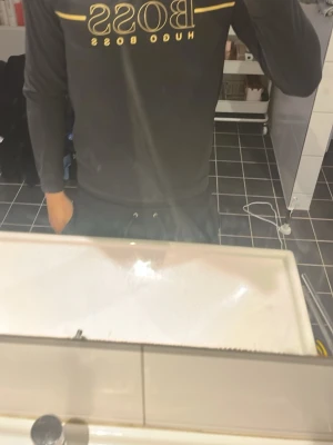 Svart långärmad tröja Hugo Boss - Snygg svart långärmad tröja från Hugo Boss med stort guldfärgat logotryck över bröstet. Tröjan har en klassisk passform och är perfekt för dig som gillar stilrena och trendiga plagg. Materialet ser ut att vara mjukt och bekvämt.