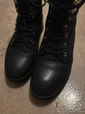 Svarta snörade kängor i skinn - Snygga svarta kängor med snörning och metallhål för snören. Tillverkade i slätt skinn med rund tå och robust sula. Perfekta för en cool och stilren look.