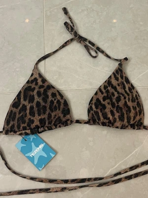Glittrig Leopardmönstrad bikiniöverdel Tezenis - Snygg glittrig trekantsbikini från Tezenis med leopardmönster i bruna och svarta toner. Klassisk modell med knyt i nacke och rygg, perfekt för sommaren. Prislappen är kvar 
