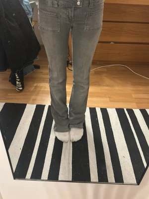 Gråa bootcut jeans med fickor - Snygga gråa jeans med bootcut-modell och stora framfickor. Jeansen har en klassisk femficksdesign och raka ben med lätt utsvängning nertill. 