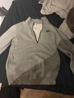 Grå halvzip sweatshirt från Nike - Säljer en grå sweatshirt från Nike med halv dragkedja och hög krage. Tröjan har en enkel och clean design med Nike-logga broderad på bröstet. Mjuk insida och ribbade muddar vid ärmslut och nederkant. Perfekt för chill dagar.