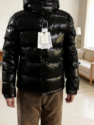 Svart pufferjacka från Moncler - Snygg svart pufferjacka från Moncler med glansig finish och huva. Jackan har dragkedja framtill, två snedställda fickor och en ficka med Moncler-logga på ärmen. Perfekt för kalla dagar och riktigt trendig look.Also have other sizes (1, 2, 3size).