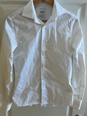 Klassisk vit skjorta från Oscar of sweden - Säljer en klassisk vit skjorta från oscar of sweden med lång ärm och knappar framtill. Skjortan har en stilren design och är tillverkad i bomull. Perfekt till många olika looks och enkel att styla.