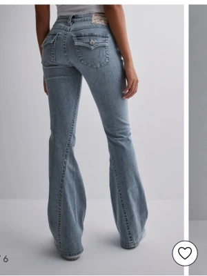 Ljusblå low rise flare jeans från true religion  - Ljusblå jeans med klassisk femficksmodell och utsvängda ben. Jeansen har en något tvättad look och silverfärgade knappar och nitar. Materialet är mjukt denim i bomull, perfekt för en avslappnad stil. Det finns små defekter längst ner som man ser på bilderna men inget annat, använt ungefär tio gånger 