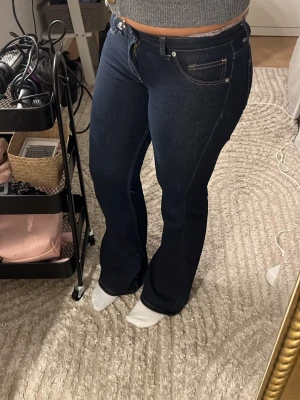 Mörkblå bootcut jeans med kontrastsömmar - Säljer ett par lågmidjade mörkblå bootcut jeans med snygga kontrastsömmar och klassisk femficksdesign. Jeansen har hög midja och är tillverkade i stretchigt denimtyg som sitter bekvämt. Perfekta för dig som gillar en tidlös och trendig look. Köpte på Sellpy men dom är ifrån hm 