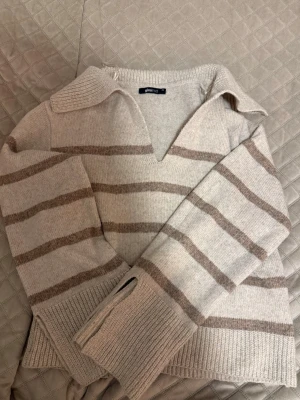 Beige stickad tröja med krage - Stickad tröja från Gina Tricot i beige med breda ljusbruna ränder. Tröjan har en djup v-ringning, krage och långa ärmar med ribbade muddar. Perfekt för lager på lager och en avslappnad look.