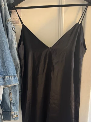 Svart nattlinne - En stilren svart nattlinne med tunna axelband och v-ringning. Klänningen har en rak passform och är tillverkad i ett glansigt material som ger en elegant look. Hör av dig vid frågor ❤️
