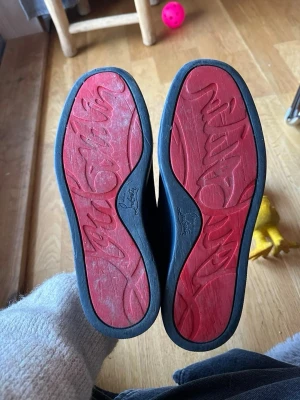 Mörkblå sneakers från Louboutin - Snygga mörkblå sneakers från Christian Louboutin i mocka med klassiska röda sulor och svarta detaljer. Skorna har rund tå, snörning framtill och diskreta sömmar som ger en clean look. Perfekta för dig som vill ha något exklusivt och stilrent. Pris kan diskuteras!!