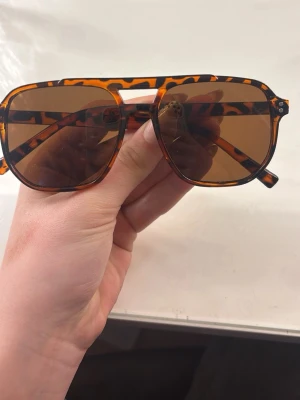 Grish solglasögon  - Snygga solglasögon med leopardmönstrad båge i brunt och svart. Modellen har stora, fyrkantiga glas och bruna linser som ger en cool retrovibe. Perfekt accessoar för att lyfta din stil i solen.