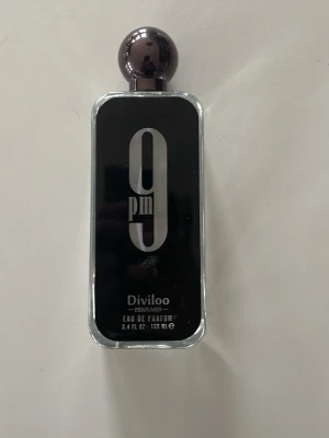 Diviloo 9pm Eau de Parfum 100ml - Diviloo 9pm Eau de Parfum i en stilren, rektangulär glasflaska med svart front och stor silverfärgad text. Flaskan har en rund, mörk kork och rymmer 100 ml. Perfekt för dig som gillar moderna och eleganta dofter. OBS!! Ca 85% kvar.