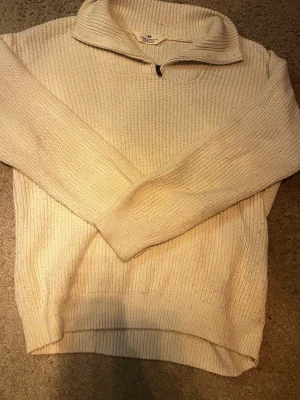 Beige stickad tröja med halv dragkedja - Stickad tröja från H&M i beige färg med ribbad struktur. Tröjan har en hög krage med halv dragkedja och långa ärmar. Perfekt för lager på lager och enkel att matcha med olika outfits.