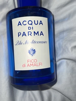 Acqua di Parma Fico di Amalfi parfym - Fräsch parfym från Acqua di Parma, Blu Mediterraneo-serien, doften Fico di Amalfi. Flaskan är i klarblått glas med vit etikett och blå text, cylinderformad med matchande blått lock. Perfekt för dig som gillar fruktiga och fräscha dofter.   Det är ungefär 1/3 kvar i flaskan