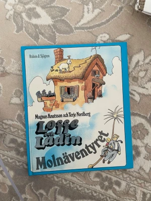 Loffe och Ladin: Molnäventyret - En färgglad barnbok med hårda pärmar, illustrerad framsida med ett hus, getter och karaktärer. Boken är skriven av Magnus Knutsson och Terje Nordberg och ingår i Klumpe Dumpe-serien. Perfekt för dig som gillar roliga och fantasifulla äventyr.