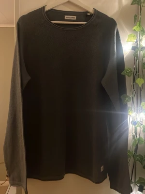 Mörkgrå tröja från Jack & Jones - En stilren mörkgrön tröja från Jack & Jones med rund halsringning och diskret struktur i materialet. Tröjan har långa ärmar och en klassisk passform som funkar till många olika looks. Perfekt basplagg för garderoben.