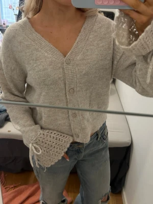 Beige kofta med virkade ärmar - Mysig beige kofta med v-ringning och knappar framtill. 