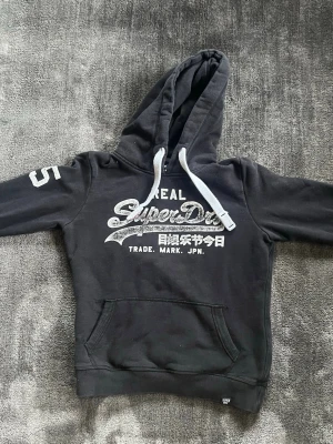 Svart Superdry hoodie - Svart hoodie från Superdry med vitt tryck på bröstet och japanska tecken. RIKTIGT liten i storleken, så det är mer som en xs, perfekt till någon som vill rocka en mer archive style. 