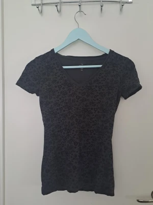 Svart t-shirt med mönster - Snygg svart t-shirt med mönster på framsidan och v-ringning. Fint skick, hittar inga defekter. 🩷