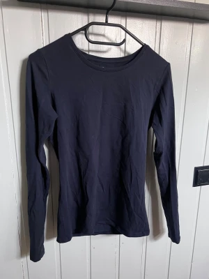 Marinblå långärmad topp i bomull - En enkel och stilren marinblå långärmad topp i mjuk bomull. Modellen har rund halsringning och en normal passform, perfekt att matcha med jeans eller kjol för en clean look.
