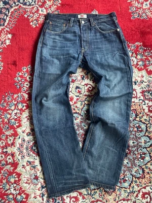 Levi's 501 blå raka jeans W29 L30 - Vintage Levi's 501 jeans i mörkblå denim med raka ben. Jeansen har en knappgylf och kontrastsömmar. Materialet är robust bomullsdenim.