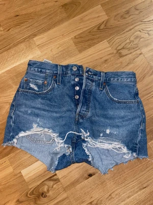 Levi's blå jeansshorts med slitningar - Säljer ett par klassiska blå jeansshorts från Levi's i strl W28