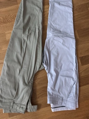 Två par byxor  i grön och blå.  - Säljer två par chinos, ett i ljusgrönt och ett i blått . Båda har klassisk rak passform, sidfickor och bälteshällor. Perfekta för en clean och stilren look. Materialet är mjukt och bekvämt, troligtvis bomull. Märke syns ej tydligt men storlek 36.