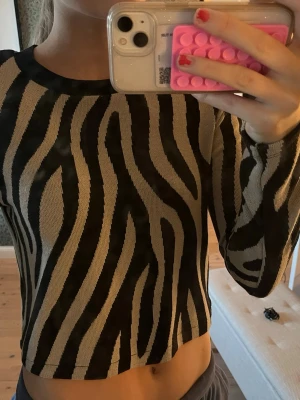 Zebramönstrad långärmad tröja - Snygg zebramönstrad tröja med svart och beige mönster. Tröjan har långa ärmar, rund halsringning och är något croppad i modellen. De är axlar vaddar i men går att ta bort.