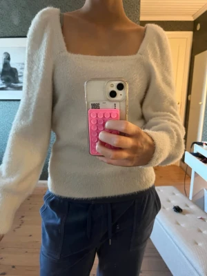 Vit fluffig stickad tröja - Mysig vit stickad tröja med fluffig textur och fyrkantig urringning. Tröjan har långa ärmar med lätt puff vid axlarna och sitter kroppsnära. Perfekt för dig som gillar en trendig och bekväm look.