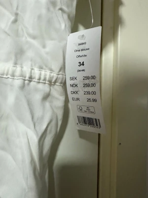 Vit blus med knappar från Gina Tricot - Snygg vit blus från Gina Tricot med korta ärmar och v-ringning. Blusen har knappar framtill och ett knytband i midjan för en avslappnad look. Tillverkad i ett lätt och luftigt material, perfekt för varma dagar.