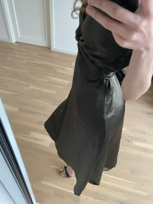 Mörkgrön omlottklänning i satin - Snygg långklänning i mörkgrön satin med omlottdesign och smala axelband. Klänningen har en elegant glansig yta och markerad midja som ger en smickrande siluett. Perfekt för dig som gillar stilrena och trendiga plagg. Storlek S