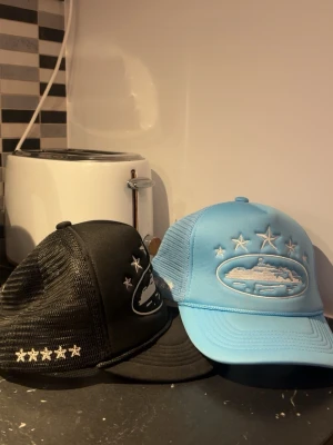 Corteiz keps - Två snygga truckerkepsar från Corteiz som passar alla skallar, en i svart och en i ljusblå. Båda har mesh på sidorna och broderade stjärnor samt  logo på framsidan. Justerbar storlek baktill och broderad logga på sidan. Perfekt för dig som gillar streetwear och vill sticka ut. Givetvis Äkta köpta från CRTZ.RTW!