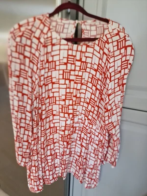 Blus från Dobber - Snygg blus från Dobber med vitt och rött grafiskt rutmönster. Modellen har rund halsringning och knappdetalj i nacken. Långärmad och tillverkad i mjukt tyg.