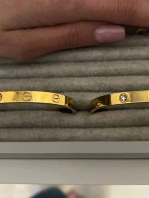 Två guldfärgade armband med stenar - Snyggt guldfärgat armband i metall med ikoniska skruvdetaljer och infällda klara stenar. Stilren och modern design som passar perfekt till din accessoarsamling. Båda är storlek s/16cm. Säljer båda för priset av en.