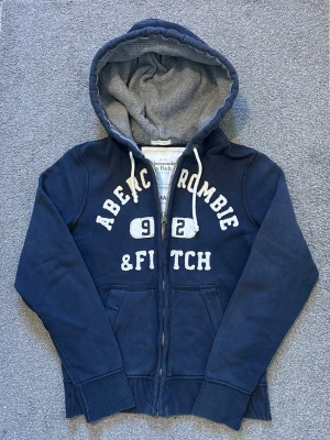 Vintage Abercrombie & Fitch Zip-Hoodie - Säljer denna riktigt snygga Abercrombie & Fitch koftan | Storlek S | Mycket bra skick | Längd≈65cm, Bredd armhåla-armhåla≈52cm | Model 175cm, 68kg | Hör av vid funderingar!