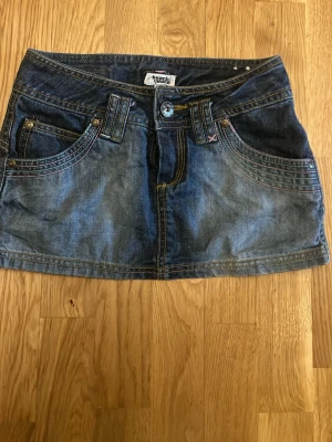 Blå jeanskjol med fickor - Snygg blå jeanskjol från Miss Sixty med klassisk femficksdesign, bälteshällor och knappstängning framtill. Kjolen har dekorativa sömmar och bakfickor med detaljerade stickningar. Perfekt för en trendig och avslappnad look.