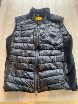 Svart dunväst från Parajumpers - Cool svart dunväst från Parajumpers med quiltad framsida och meshpaneler på sidorna. Västen har en gul detalj vid kragen, bröstficka med dragkedja och en bakficka med zip. Perfekt för lager-på-lager och outdoor. Den har 2 små hål men inget man tänker på