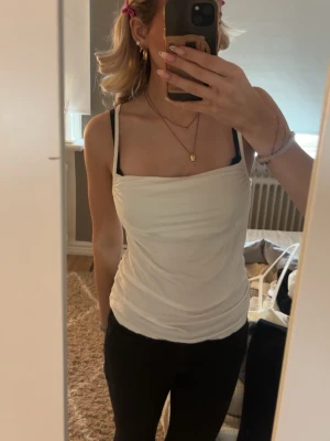 Vit linnetopp med smala axelband - Snygg vit linnetopp med smala axelband och draperad halsringning från Nelly. Väldigt skönt material, använd fåtal gånger, inga defekter. Skriv om ni har frågor💕