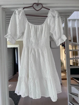 Vit broderad kortklänning med puffärm - Söt vit kortklänning med broderade detaljer och puffärmar. Klänningen har en öppen rygg med knytband och volang nertill. Perfekt till skolavslutning, student, konfirmation mm.  Liten gul fläck (se sista bilderna) men annars fint skick🫶🏻