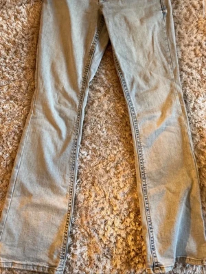Ljusblå bootcut jeans - Säljer ett par ljusblå bootcut jeans med klassisk femficksdesign och normal midja. Jeansen har en avslappnad passform och är tillverkade i denim med lätt tvättad look. Perfekta för en casual och trendig stil.