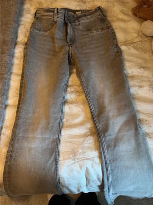 Grå flared jeans från H&M - Säljer ett par gråa flared jeans från H&M med justerbar midja och låg midja. Jeansen har klassisk femficksdesign och är tillverkade i bomullsmix. Perfekta för dig som gillar en avslappnad men trendig look.