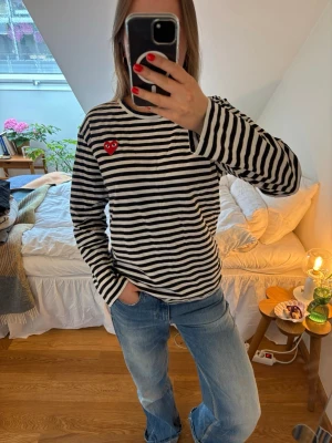Randig långärmad tröja Comme des Garçons - Säljer en svartvit randig långärmad tröja från Comme des Garçons med det ikoniska röda hjärtat med ögon broderat på bröstet. Tröjan har rund hals och är gjord i mjukt bomullsmaterial. Perfekt för dig som gillar stilrena och coola plagg. Storleken är i L men passar mig som har s/m. 
