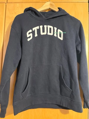 Mörkblå hoodie från Jack & Jones -  en mörkblå hoodie från Jack & Jones med STUDIO-tryck i vitt på bröstet. Perfekt för dig som gillar en avslappnad och cool stil. Lite noppig 164 barnstorlek 