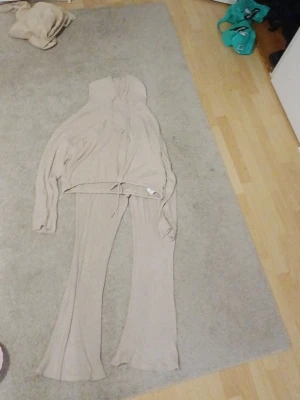 Beige ribbat loungewear-set Gina Tricot - Mysigt loungewear-set från Gina Tricot i beige ribbat material. Setet består av en hoodie med dragsko och matchande utsvängda byxor. Perfekt för chill dagar hemma. Materialet är mjukt och stretchigt för extra komfort.