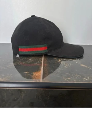 Svart keps från Gucci med röd/grön detalj - Snygg svart keps från Gucci med diskret GG-mönster i tyget och klassisk röd/grön rand på sidan.                                                                                        Kan gå ner i pris vid snabb affär ✅