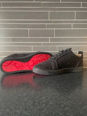 Svarta Loubs utan spikar - Snygga svarta sneakers i mocka och textil. Skorna har klassisk låg profil, svarta snören och den ikoniska röda sulan med logotyp. Perfekta för dig som vill ha en stilren och exklusiv look. Storlek 43 på skorna och använda 3 gånger. Hör av dig 🤙 