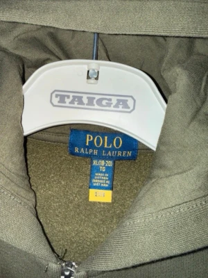 Olivgrön hoodie från Polo Ralph Lauren - Säljer en olivgrön hoodie från Polo Ralph Lauren med dragkedja framtill och klassisk huva. Hoodien är tillverkad i mjukt material och har en enkel, stilren design utan tryck eller mönster. Perfekt för en avslappnad och cool look. Passar storlek S. Pris kan absolut diskuteras.