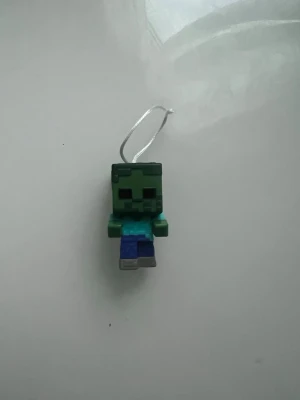 Kinder joy - Minecraft zombie mobilhängare - Cool mobilhängare i form av en zombie från Minecraft. Figuren är grön och blå med pixel-design och har en liten snodd för att fästa på mobilen eller nyckelringen. Tillverkad i plast och perfekt för dig som gillar gaming och vill pimpa din mobil.